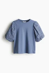 Top azul de punto de algodón con cuello redondo y bajo recto. Mangas globo cortas en tejido de algodón con forro de punto y ribete elástico.