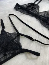 Conjunto de lencería negro de encaje, compuesto por un corpiño tipo bralette, una tanga de tira doble regulable, un portaligas desmontable y ligas regulables.