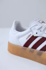Zapatillas Adidas Samba de cuero blanco con puntera de gamuza gris y tres tiras de cuero bordó. Suela de goma color caramelo traslúcida.