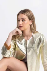 Chaqueta corta dorada de cuero sintético, corte recto, estilo Chanel y mangas 3/4 con puños marrones.