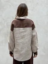 Camisa beige a rayas verticales finas, con cuello clásico, mangas largas abullonadas con puños marrones y cierre frontal con botones.