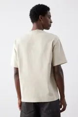 Remera color beige de algodón pesado, corte holgado, cuello redondo ribeteado, hombros caídos y bajo recto.