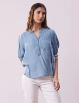 Blusa celeste de lyocell, con cuello a la base, escote en V y botones. Delantera con bolsillo y manga corta con terminación en punto smock.