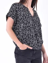 Blusa negra con estampado floral en tonos claros, de corte suelto y mangas cortas.