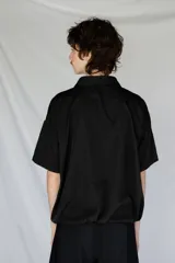 Remera oversize negra de piqué de algodón con bolsillo estampado con una palmera Phoenix Canariensis. Tiene elástico verde con hebilla de ajuste en la parte inferior.