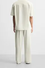 Pantalón relaxed fit de color beige con finas rayas verticales, confeccionado en una mezcla de algodón y cáñamo. Presenta cintura elástica, bolsillos laterales, un bolsillo trasero de plastrón y cierre frontal con botones.