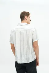 Camisa de manga corta confeccionada en lino y algodón a rayas verticales en tonos blanco, gris y beige. Tiene cuello tipo cubano, corte regular y logo bordado en el pecho.