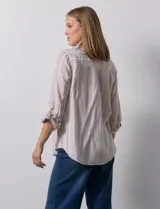 Camisa color beige con rayas verticales blancas, de lino, con cuello con solapa y abertura central con botones. Tiene un bolsillo aplicado en el pecho y mangas largas regulables con presilla y botón.