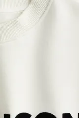 Buzo de tejido de punto color blanco roto, con cuello redondo, hombros caídos y puños y bajo acanalados. Presenta un estampado frontal en negro con el texto "LE MAISON de Paris".