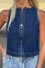 Top sin mangas de denim azul con cierre metálico dorado frontal y tirador circular. Corte recto y escote redondo.