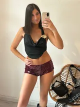 Top negro con escote drapeado, espalda descubierta y detalle de broche dorado en el hombro.