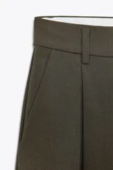 Pantalón de vestir color verde oscuro, de tiro alto con trabillas y pinzas delanteras. Presenta bolsillos laterales y falsos bolsillos traseros de vivo.