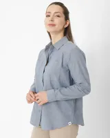 Camisa celeste de manga larga confeccionada en algodón chambray, con cuello clásico, cierre frontal con botones, dos bolsillos de parche en el pecho y corte relajado.