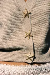 Chaqueta amarilla de punto con escote de pico y manga corta. Cierre frontal con botones en forma de estrella.