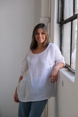 Blusa blanca de lino con cuello redondo y mangas 3/4 con botón. Tiene un bolsillo en el pecho con bordados.