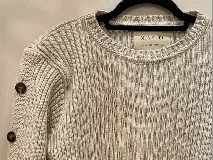 Sweater de punto color beige, con cuello redondo, textura acanalada y botones decorativos en las mangas. Hecho en Uruguay.