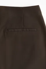 Short pollera marrón con corte mini, de tiro alto, con cierre lateral oculto y bolsillo decorativo trasero.