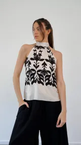 Top de seda color crema con estampado de flores negras, cuello halter y lazo en la espalda.