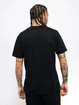 Remera amarilla con una franja vertical negra en el lado izquierdo. En la parte superior de la franja se encuentra el escudo del Club Atlético Peñarol. En la parte inferior de la franja se lee la leyenda "Oro y Carbón".