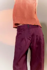 Pantalón de lino color marrón, con corte tipo barrel, tiro medio, pretina ancha con doble abotonadura, bolsillos laterales y pinzas en el frente. Ruedo con presilla permitiendo usarlo recto o fruncido al tobillo.