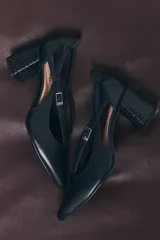 Zapato de tacón negro de charol con punta fina, tiras delgadas entrecruzadas sobre el empeine y hebilla plateada lateral. Tacón de bloque texturizado.