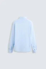 Camisa celeste a rayas verticales blancas, de corte recto, con cuello italiano abierto, mangas largas con puños abotonados y cierre frontal con botones.