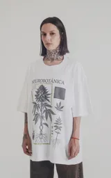 Remera blanca de algodón con cuello redondo y calce oversize. Estampa frontal con diseño de planta de cannabis, texto "Neurobotánica" y patrón geométrico.