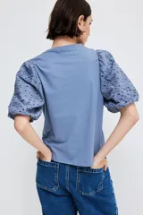 Top azul de punto de algodón con cuello redondo y bajo recto. Mangas globo cortas en tejido de algodón con forro de punto y ribete elástico.