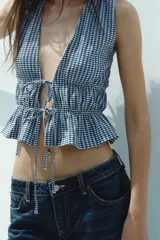 Top amarillo con estampado de cuadros vichy blancos, escote en pico, sin mangas, con detalle de elásticos en la cintura y cierre frontal con lazadas.