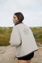 Campera de algodón color beige claro, con cuello y ribetes en color marrón oscuro. Presenta un bordado grande en la espalda con iniciales entrelazadas. Tiene un calce amplio y mangas anchas.