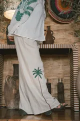 Pantalón de lino color crudo con corte amplio y estampado de palmeras en la parte inferior de las piernas.