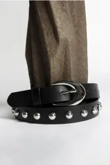 Cinturón negro de cuero sintético con tachas plateadas y hebilla metálica plateada.