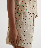 Blusa de crepé color beige con estampado de lunares de colores, cuello redondo con ribete negro, manga corta abullonada, bolsillo de parche en el pecho y bajo mullet con aberturas laterales.