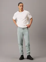 Pantalón de chándal de felpa color verde agua, con cintura elástica ajustable con cordón, puños de canalé, bolsillos laterales y trasero, y logo bordado de Calvin Klein en la pierna.