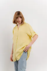 Camisa amarilla de lino con corte recto y calce suelto. Tiene cuello camisero, botones en el frente y mangas cortas con presilla y botón.