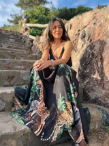 Vestido largo negro con estampado de jungla con palmeras, jirafas y leopardos. Tiene breteles finos, escote en V cruzado y cinturón con apliques brillantes.