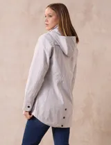 Campera impermeable color gris claro, marca Gallery. Tiene abertura central con cierre oculto y botones a presión, bolsillos delanteros y capucha plegable en el cuello.