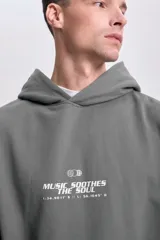 Canguro gris con capucha, cordón ajustable, bolsillo tipo canguro y puños y cintura acanalados. Estampa frontal con la frase "Music Soothes the Soul" y coordenadas.