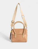 Cartera tipo city color beige, de tela deportiva, con doble asa corta, correa regulable desmontable, solapa con broche a presión y charm colgante.