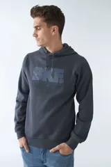 Buzo canguro color arena de felpa, con capucha ajustable, bolsillo tipo canguro, mangas largas y logo estampado en el pecho.