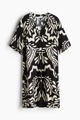 Vestido túnica corto de viscosa con estampado abstracto en blanco y negro, cuello mao con abertura en V, mangas cortas, corte holgado, hombros caídos y tajos laterales. Espalda ligeramente más larga.