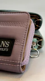 Billetera corta con cierre alrededor y tapa, confeccionada en tela capitoneada. Incluye varias reparticiones con tarjeteros y bolsillos internos, y una correa de mano desmontable. Disponible en negro, rojo y dorado.