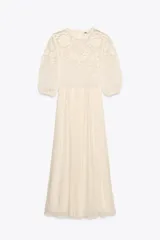 Vestido midi color crudo, con cuello redondo y mangas tres cuartos con elástico. Presenta combinación de tejidos y bordados a tono.