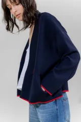 Chaqueta de punto color crudo con solapa ancha acanalada terminada con cadenetas en contraste negro. Tiene calce relajado, hombros caídos, largo a la cadera y manga larga.