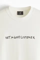 Remera blanca de corte holgado con cuello redondo y estampado con la frase "NOT A GOOD LISTENER" en letras negras.