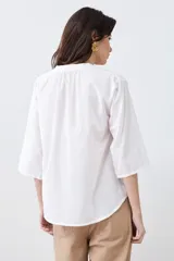 Blusa blanca con cuello mao y mangas 3/4. Presenta apliques circulares bordados en el frente.