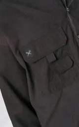 Camisa negra de manga larga, estilo técnica con múltiples bolsillos delanteros y un bolsillo en la parte inferior de la espalda, botones en cartera y mangas, calce oversize, confeccionada en textil ligero suave al tacto.