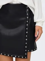 Minifalda negra de cuero sintético con corte cruzado y tachas plateadas en forma de estrella.