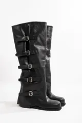 Botas altas color marrón claro, de cuero gamuzado, con caña alta y múltiples correas horizontales con hebillas metálicas.