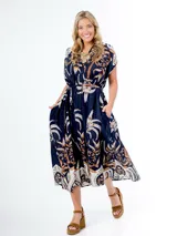 Vestido midi de algodón italiano, color azul marino con estampado en tonos blanco, beige y naranja/marrón. Presenta mangas cortas tipo murciélago, cuello en V con botones frontales y lazo desmontable para ajustar a la cintura.